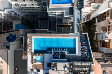 Hava görüntüsü Mellieha 'yı, Malta' daki çatı havuzlarını, tahta döşemeleri, gri fayansları ve güneşlikleri gösteriyor. Gün ortası ışığı küçük bir şehir şebekesinde taze gölgeler oluştururken insanlar rahatlıyor..