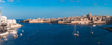 Valletta 'nın hava manzarası, Malta' da güçlendirilmiş kireçtaşı duvarlar, bazilika kubbesi ve Grand Harbour 'daki sıcak tonlu tekneler ve derin mavi sularla dolu tekneler görülüyor..