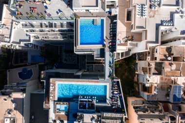 Havadan bakıldığında Mellieha, Malta 'daki modern bloklarda iki çatı havuzu görünüyor. Havuz güvertesindeki insanlar, şezlonglar, havalandırma üniteleri ve gündüz gölgeleri bir ızgara oluşturuyorlar.