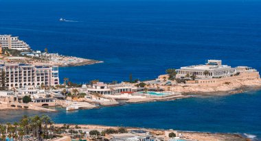 Sliema, Malta 'nın havadan görünüşü, modern deniz manzaralı oteller, teraslı binalar, kayalık koylar, parlak öğle vakti ışığında lidolar, turkuaz sığ ve katıksız kireç taşı.