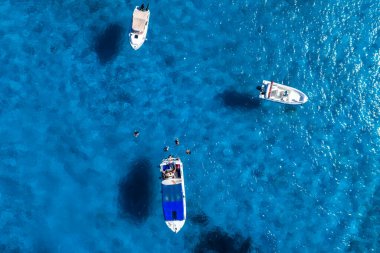 Havadan bakıldığında Mavi Göl, Comino Adası, Malta görünüyor. Turkuaz sığ sularda yüzen üç tekne ve gün ışığında yüzen şnorkeller gibi karanlık yamacalar..