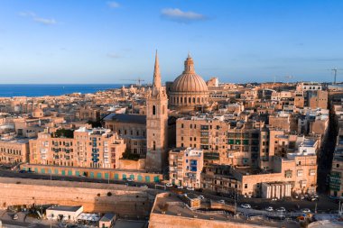 Gün batımında Valletta, Malta 'nın havadan görünüşü, bazilika kubbesi ve katedral kulesi kireçtaşı caddelerin ve kalelerin üzerinde yükseliyor, altın saat ışığı deniz kenarında kumtaşlarını ısıtıyor..