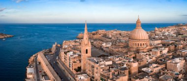 Hava manzarası günbatımında Valletta Malta 'yı gösteriyor, bazilika kubbesi ve katedral kulesi kireç taşı blokları ve kale duvarları üzerinde, sakin Akdeniz mavisi yelkenlileri.