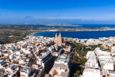 Hava görüntüsü, Mellieha, Malta 'da beyaz binaların üstündeki kırmızı kumtaşı kilise, Mellieha Körfezi, Comino ve Gozo' yu gösteriyor..