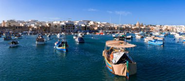 Düzinelerce luzzu teknesi Marsaxlokk, Malta 'da turkuaz suyla sallanırken, Pompei Leydisinin Kilisesi sağa doğru yükseliyor.