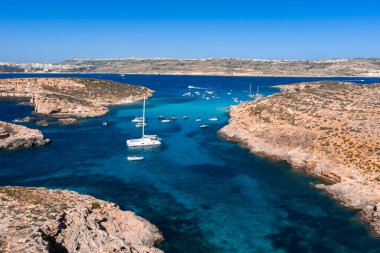 Hava görüntüsü Malta 'nın Comino Adası' ndaki Mavi Göl 'ü gösteriyor. Turkuaz sığlıklar, kireçtaşı uçurumları, Cominotto yakınlarındaki tekneler ve açık gün ışığında Malta ufkunda..