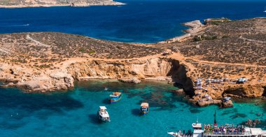 Comino, Malta 'daki Mavi Göl' ün hava manzarasında parlak bir yaz gününde turkuaz sığlıklar, bal renkli kayalıklar, kayıklar, yüzücüler, kumlu koylar ve deniz mağaraları görülüyor..