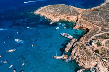Hava görüntüsü, Malta, Comino Adası 'nda Mavi Göl' ü, turkuaz suyu, kireç taşı kayalıkları, kurak çalılıklar, tekne ve tur gemileri, dar körfez, kaya terasları, yaya yolları gösteriyor..