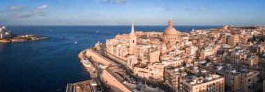 Hava manzarası, gün batımında Valletta Malta 'yı, Grand Harbour' u, Bazilika Kubbesi 'ni ve St. Pauls Pro Katedrali' ni, sakin sulardaki tekneleri, ılık ışığı, uzun gölgeleri gösteriyor..