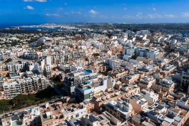 Mellieha, Malta 'nın havadan görünüşü, kireçtaşı binalar, modern bloklar, teraslar, havuzlar ve kavisli koylar. Comino ve Gozo gün ışığında uzakta görünüyorlar..