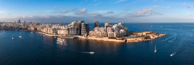 Gün batımında Malta 'nın hava manzarasında Marsamxett Limanı' ndan Aziz Julians ve Sliema, modern deniz kenarı kuleleri, eğri gezinti güvertesi ve derin mavi suyu geçen yelkenliler görülüyor..
