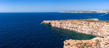 Hava görüntüsü Malta 'daki Comino Adası' nı gösteriyor. Mavi Göl yakınlarında kireçtaşı kayalıkları, koyları ve turkuaz sığlıkları var. Tekne uyanıyor. Gün ortası ışığı altında kanalın izini sürün..