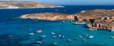 Hava görüntüsü Malta 'nın Comino Adası' nda Mavi Göl 'ü gösteriyor. Kireçtaşı kıyıları arasında turkuaz su, demirli botlar, ufukta Gozo ve Malta, parlak öğle vakti, sakin deniz..