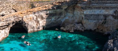Comino Adası, Malta 'daki Mavi Göl' ün havadan görünüşü. Koyda tekneler, elektrikli turkuaz su, kireçtaşı uçurumlar, deniz mağaraları ve parlak öğle vakti aydınlığında bir yığın kayık..
