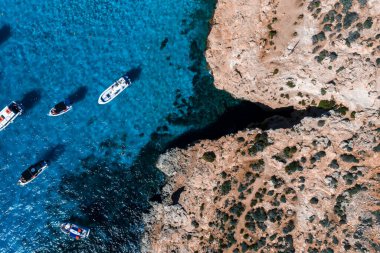 Comino Adası 'nın havadan görünüşü, Malta, Mavi Göl. Tekneler ve sürat tekneleri açık sığ sularda demirler, deniz tabanındaki gölgeler, parlak öğlen ışığı, doymuş maviler, yaz havası.