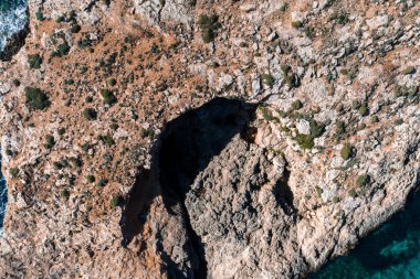 Malta 'daki Comino Adası' nın yukarıdan görünüşü Mavi Göl 'ün bir deniz mağarasını gösteriyor. Güneş ışığı kireç taşı, alçak çalılar ve sivri çatlak çizgileri parlak gün ortasında ortaya çıkar..