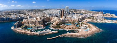 Hava görüntüsü, Malta 'daki Sliema ve St. Julians rıhtımlarını Portomaso Marina ve Portomaso İş Kulesi, kireçtaşı binalar, rıhtımlar ve gün ortası aydınlığıyla gösteriyor..