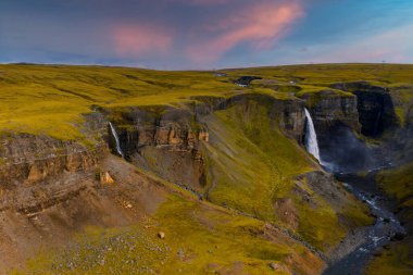 Hava görüntüsü Haifoss 'u ve Thjorsardalur, güney İzlanda' da daha küçük bir düşüşü gösteriyor. Altın saat ışığı bazalt kayalıkların, yosunlu bozkırların ve dolambaçlı bir nehrin üzerinde uzun gölgeler oluşturur..