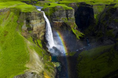 Hava görüntüsü Haifoss şelalesinin İzlanda 'nın güneyindeki engebeli bir kanyona düştüğünü gösteriyor. Siste bir gökkuşağı kavisleri, bazalt katmanları göze çarpıyor, ve yaz güneşinde aşağıda bir nehir esiyor..