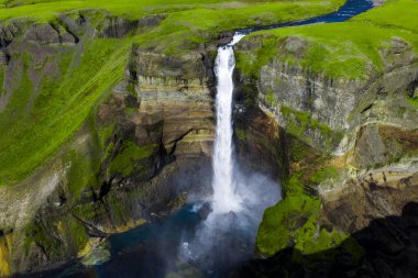 Hava görüntüsü Haifoss şelalesinin İzlanda 'nın güneyindeki sisli bir havuza düştüğünü gösteriyor. Parlak gün ortası ışığı, katmanlı volkanik kayayı ve aşağıdaki turkuaz havuzu ortaya çıkarıyor..