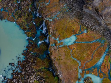 Koyu volkanik kaya ve yosun üzerindeki süt mavisi buzul akıntılarının havadan görünüşü, küçük şelaleler turkuaz nehirlerini paslı turuncu tundralardan İzlanda 'daki mat bir lagüne doğru besler..