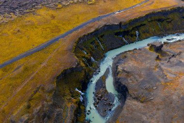 İzlanda Dağları 'ndaki Sigoldugljufur' un hava manzarası koyu mavi bir buzul nehrinin bazalt kanyonu, ince şelaleler, yosunlu kayalıklar ve platoda bir yol kestiğini gösteriyor..