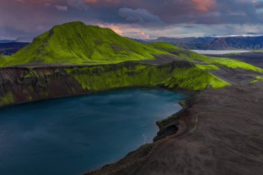 Landmannalaugar yakınlarındaki İzlanda 'da volkanik bir göl manzarası. Dik jantlarda zümrüt yosunları, siyah lav alanları, yosunlu bir dağ ve alacakaranlık ışığı zıtlıklarını vurguluyor..