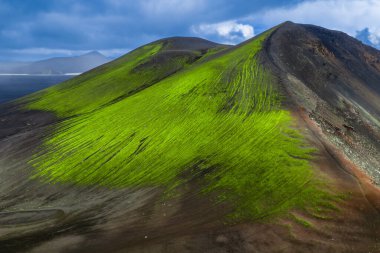 İzlanda 'daki volkanik bir tepenin havadan görünüşü neon yeşil yosun perdeleri karanlık bazalt yamaçlar, kül tarlaları ve kara kara kara bulutlar altında Landmannalaugar yakınlarındaki uzak dağlar gibi..