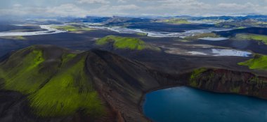 Hava görüntüsü Landmannalaugar 'daki İzlanda volkanik dağlarını gösteriyor. Yosun yeşili rhyolite tepeleri, koyu lav, buzullu nehirler ve gün ışığında kar düzlükleriyle mavi bir krater gölüdür..