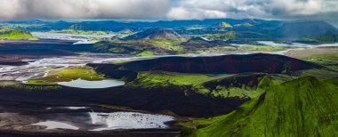 Landmannalaugar yakınlarındaki İzlanda volkanik dağlarının hava manzarası, yosunlu rhyolite tepeleri, siyah lav tarlaları, krater gölleri ve yoğun bulutların altında buzul nehirleri örülmüş..