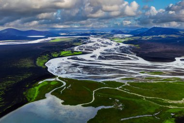 Kara volkanik kumlar üzerinde örülmüş nehrin ve İzlanda dağlık arazilerinde, Landmannalaugar ya da Thorsmork yakınlarında neon yeşil yosunların üzerindeki hava manzarası yaz sonlarında hızlı hareket eden bulutların altında..