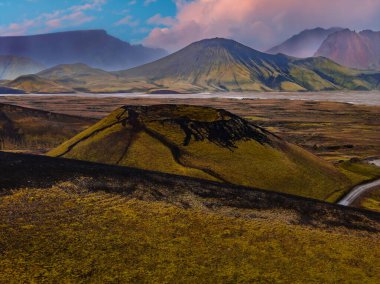 İzlanda volkanik dağlarının havadan görünüşü yosun kül kozalakları, karanlık lav akıntıları ve Landmannalaugar yakınlarında sıcak akşam ışığı altında örülmüş bir nehir..
