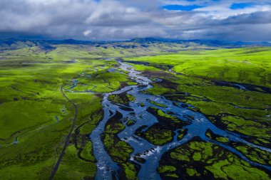 Hava görüntüsü İzlanda 'daki yosun yeşil ovalarından geçen örülmüş buzullar gösteriyor. Karanlık lav adaları, uzak dağlar ve yüksek kontrastlı gün ışığında yamalı güneş ışığı..
