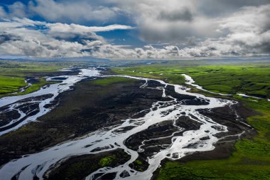 Hava görüntüsü siyah volkanik kumlar üzerinde örülmüş nehirler ve İzlanda 'nın güney kıyısında, Katla ya da Vatnajokull yakınlarında, hızlı bulutlar ve noktalı ışıkla kaplı yeşil yosunlar gösteriyor..