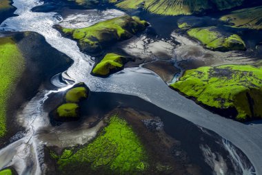 Hava görüntüsü siyah kum ve küller üzerinde örülmüş bir buzul nehrinin Landmannalaugar yakınlarındaki Landmannalaugar 'da yosun yeşili tepeler ve güpegündüz çökelti pervaneleriyle birlikte olduğunu gösteriyor..