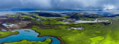 Hava görüntüsü, Landmannalaugar yakınlarındaki İzlanda dağlık bölgelerinde, yosunlu lav tarlaları, krater sırtları, göller ve nehirler gösteriyor. Fırtına bulutları ve karanlık bazalt ile canlı tundralara karşı..