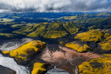 İzlanda 'da, Landmannalaugar ya da Fjallabak yakınlarında, serin gün ışığı bulutları altında yosun sarısı ve yeşil, siyah kumlar ve örülmüş nehirlerin havadan görünüşü..