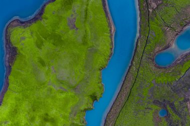 Hava görüntüsü, İzlanda 'nın Landmannalaugar veya Sigoldugljufur yakınlarındaki dağlık bölgelerindeki neon yeşil yosunlardan süzülen mavi suyu gösteriyor. Parlak gün ışığı, yüksek irtifa.
