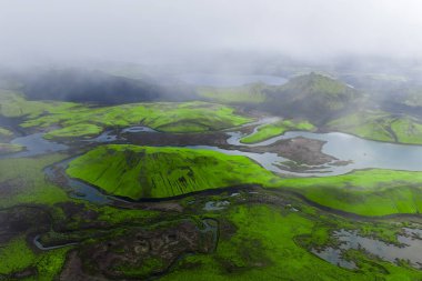 Landmannalaugar yakınlarındaki İzlanda Highlands 'ta yosun yeşili tepeler, örülmüş nehirler, lav tarlaları ve ryolite sırtları alçak bulutlar ve yayılmış gün ışığı..