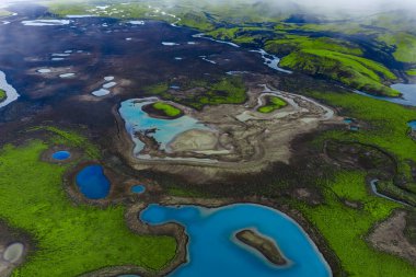 Turkuaz göller, kül gri lav tarlaları ve İzlanda dağlık kesimlerinde muhtemelen alçak bulutlar ve güneş ışığı desenleriyle Landmannalaugar veya Fjallabak gibi yeşil yosunların görüldüğü hava manzarası..