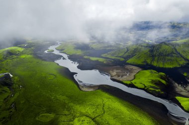 Havadan bakıldığında, Landmannalaugar ya da Sigoldugljufur yakınlarındaki İzlanda 'da yosun yeşil lav ve siyah kumlar arasında serin serin bir ışık altında bir buzul nehri görülüyor..