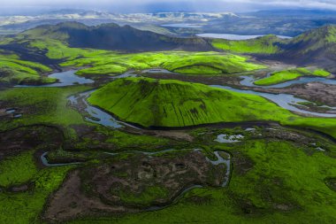 Yüksek irtifa havası yosun kaplı krater, örülmüş nehirler ve Landmannalaugar, İzlanda yakınlarındaki karanlık lav tarlaları gösteriyor. Yağmurdan sonra bulutların altında yer değiştiren bulutlar altında..