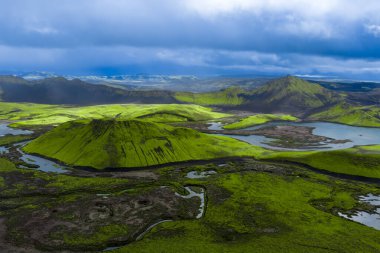 İzlanda 'daki Landmannalaugar' ın hava manzarası yosunlu tuff konileri, rhyolite tepeleri, krater gölleri, karanlık lav alanları ve yazın fırtınalı bulutların altında örülmüş nehirleri gösteriyor..
