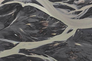 Landmannalaugar yakınlarındaki İzlanda 'da koyu volkanik kumlar boyunca uzanan soluk buzul nehirleri, yumuşak yayılmış ışıkla alüminyum zengin su ve kömür grisi desenleri ortaya çıkarıyor..