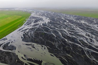 Hava görüntüsü İzlanda 'nın güneyindeki siyah bir kum ovasında sütlü kanallar gösteriyor. Tortu zengin su, serin bir günde yumuşak bulutlu ışık altında gümüş kurdeleler dokuyor..