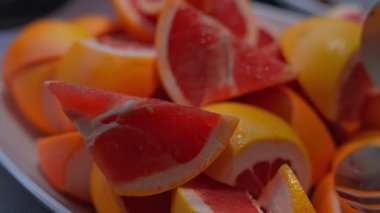 Dar makro, tepside sarı kabuklu kırmızı greyfurt kamaları, kenarda bir çatal, sıcak renk ve sığ alan derinliği, Malta 'da yumuşak doğal ışık gösteriyor.