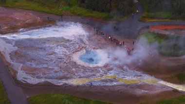 Havadan bakıldığında mavi menfez, buhar, sülfür sarısı şeritler ve sinter terasları görünüyor. Turistler Haukadalur, İzlanda 'da bulutlu bir gün ışığı altında..