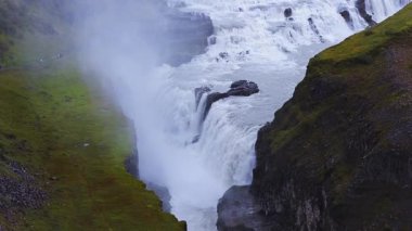 İzlanda 'daki Hvita nehri üzerindeki Gullfoss' un hava manzarası iki katlı şelale, sis, çimenli teras, taş platformlar, yosunlu yaylalar ve serin ışık altındaki karanlık bazalt kayalıklar gösteriyor..