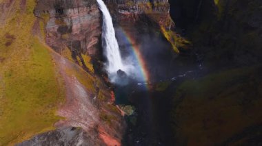 İzlanda 'daki Hayoss' un havadan drone görüntüsü su kanyona dalarken görülüyor. Yavaş süpürme bazalt, kırmızı ve gri katman, gökkuşağı, nehir ve elektrik hatlarını gösterir.