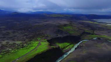 Hava manzarası karanlık düzlükler, lav tarlaları, yeşil yosun, sütlü mavi bir buzul nehri derin bir kanyonu, kraterleri, uzak dağları, kıyıları ve yolda küçük arabaları gösteriyor..